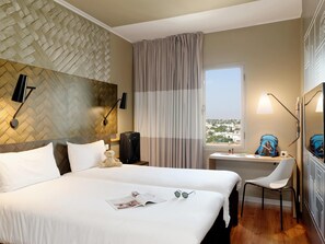 A hotel room with a large bed, a desk with a chair, a window with a view, and a wall-mounted lamp. - Hotel ibis Casa Sidi Maarouf (Casablanca)