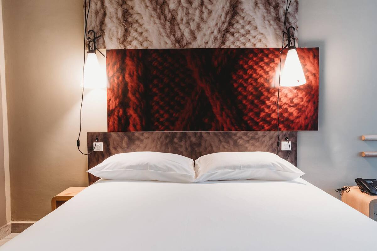 Una habitación de hotel con una cama grande, dos lámparas de noche y una obra de arte colgada en la pared.