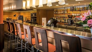 A bar area with a counter, stools, and a variety of bottles and glasses on shelves.