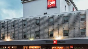 Um hotel moderno com um destaque para a placa 'ibis', apresentando um design contemporâneo e limpo, com linhas horizontais e janelas amplas.