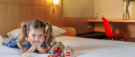 A child on a bed with a coloring set, a jar of candies, and a red 'ilbis' sign.