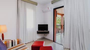 Une chambre d’hôtel équipée d’une télévision, d’un canapé, d’un pouf rouge et d’un balcon avec des rideaux.