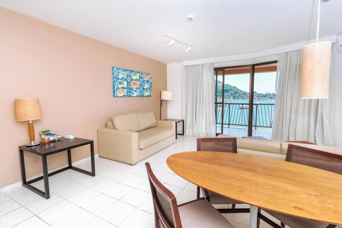 A hotel room with a sofa, a dining table, a lamp, and a painting on the wall.