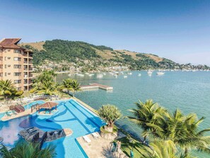 A resort with a swimming pool, palm trees, and a view of the sea and hills. - Hotel Nacional Inn Angra dos Reis (Angra dos Reis)
