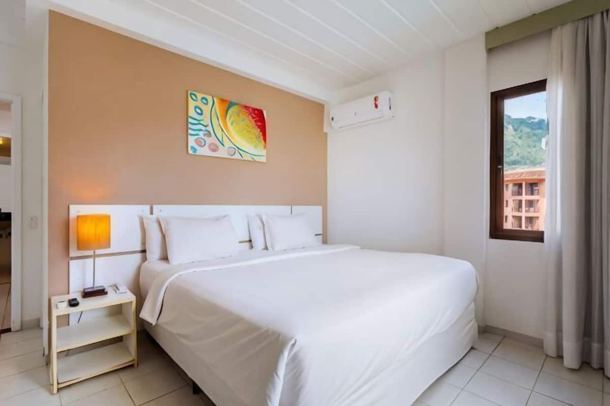 A hotel room with a bed, bedside table, lamp, and a window with curtains.