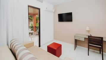 A room with a sofa, a desk, a TV, and a small red ottoman.