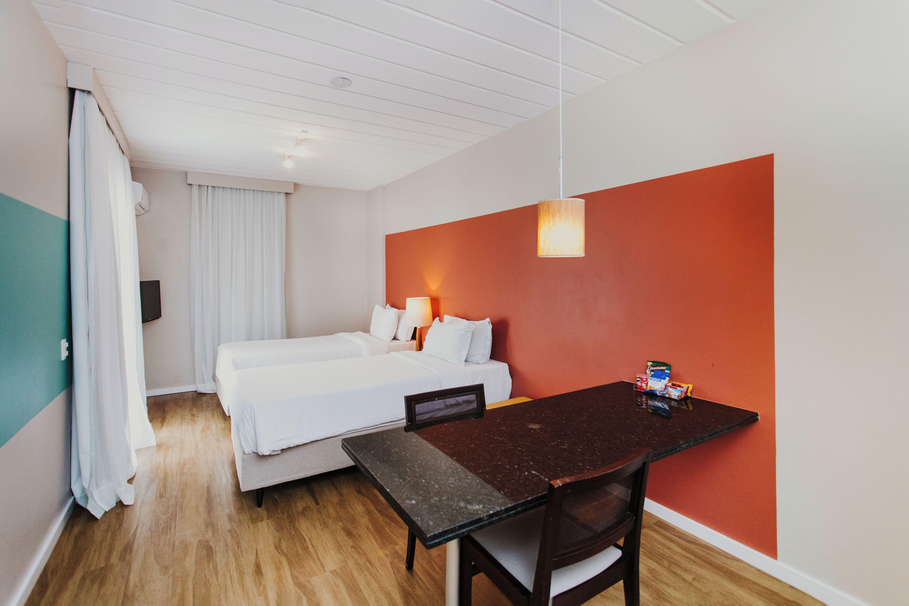 A hotel room with a bed, a desk, and a red accent wall.
