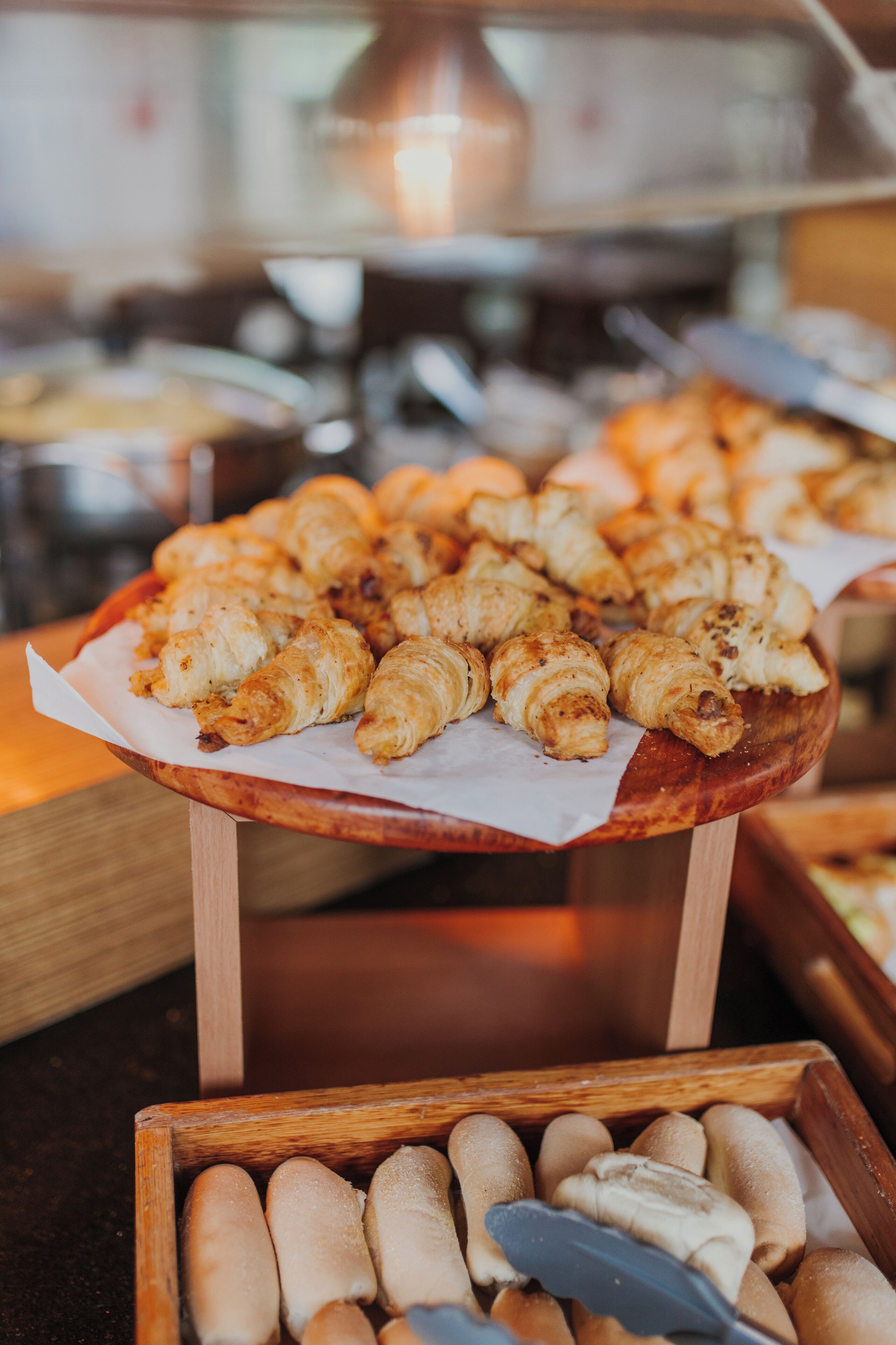 A wooden serving tray with croissants and a wooden box with breadsticks.