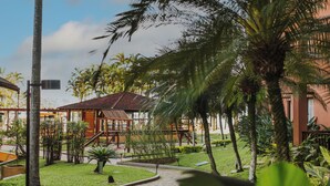 A pathway leading through a garden with palm trees and a building in the background.