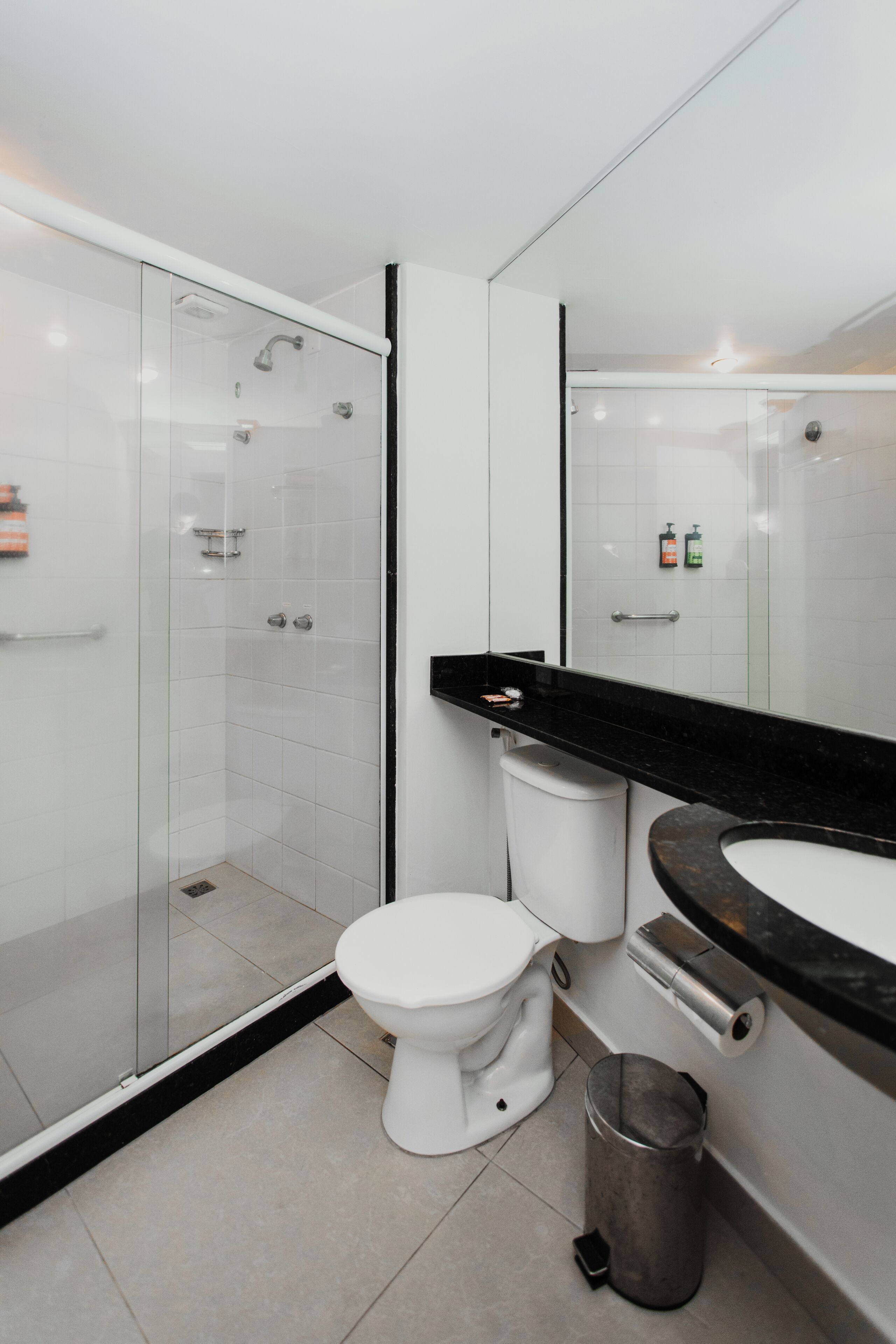 Une salle de bain moderne avec une douche à parois de verre, des toilettes blanches, un lavabo noir et une poubelle.