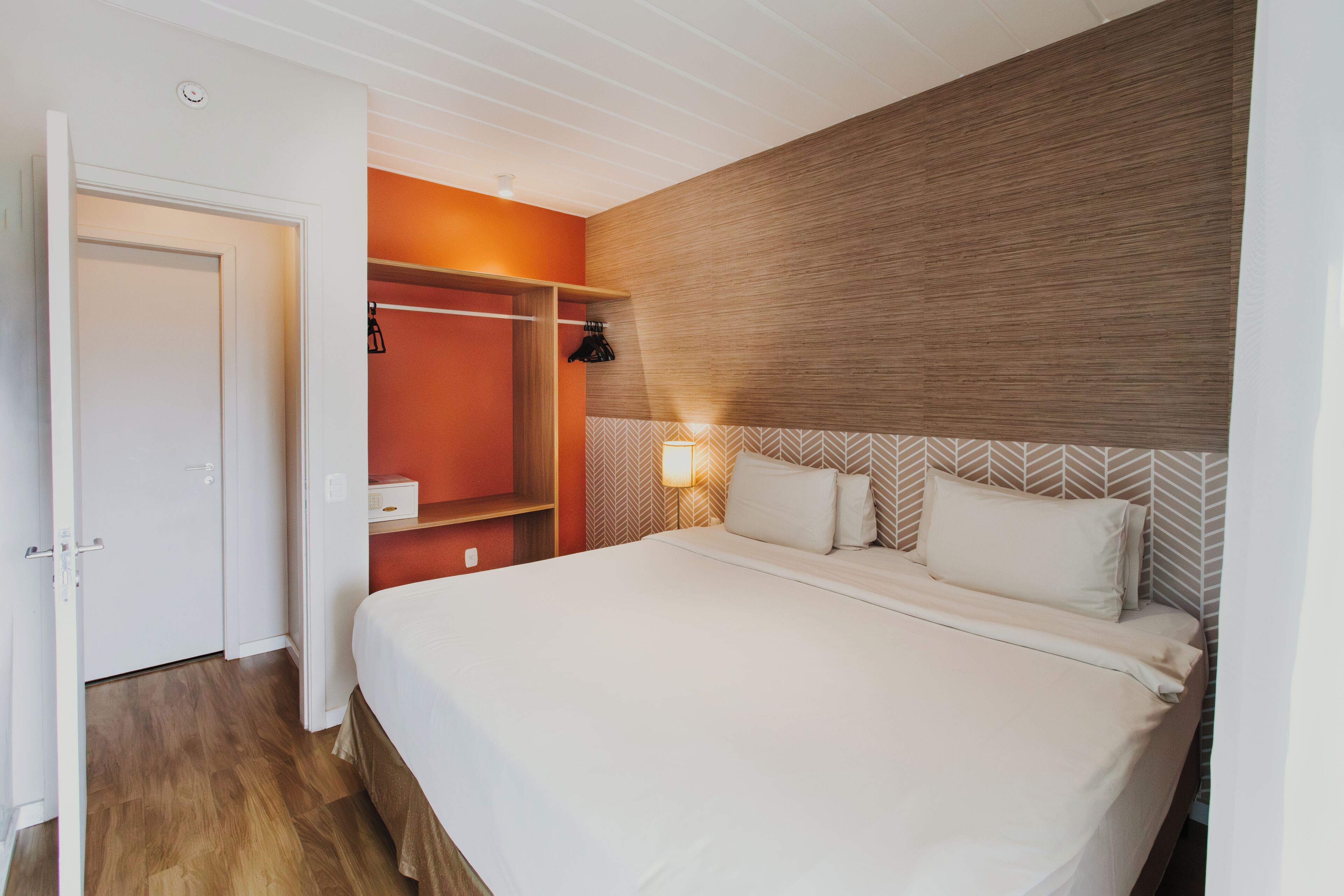 A hotel room with a large bed, a wardrobe, and a bedside table with a lamp.