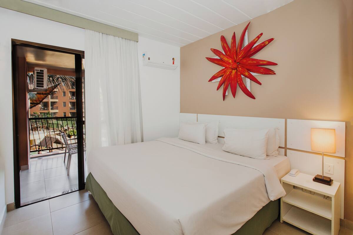 A hotel room with a bed, a nightstand, a wall-mounted lamp, and a large red flower decoration.