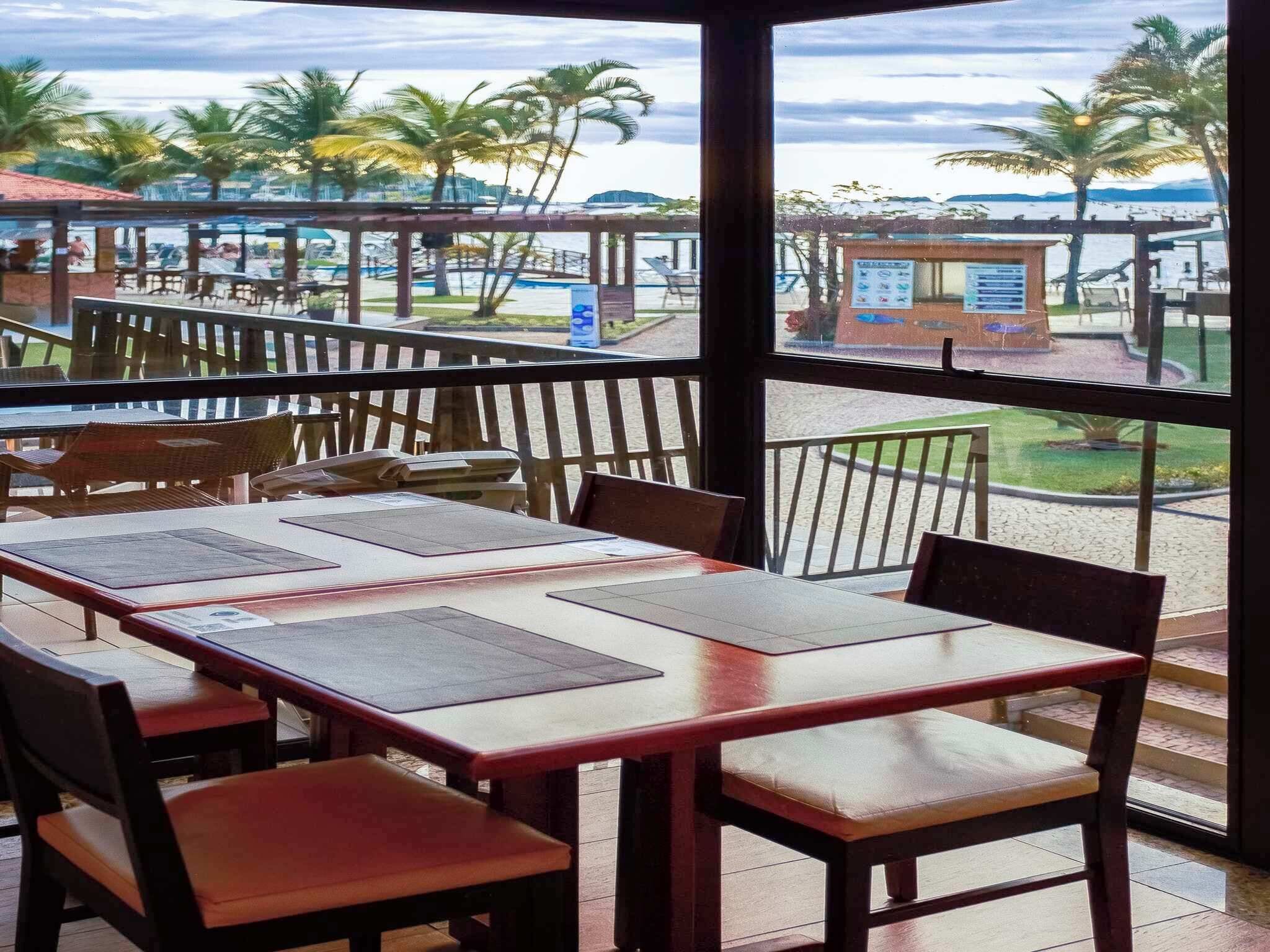 An outdoor restaurant with tables and chairs, a view of palm trees and a body of water.