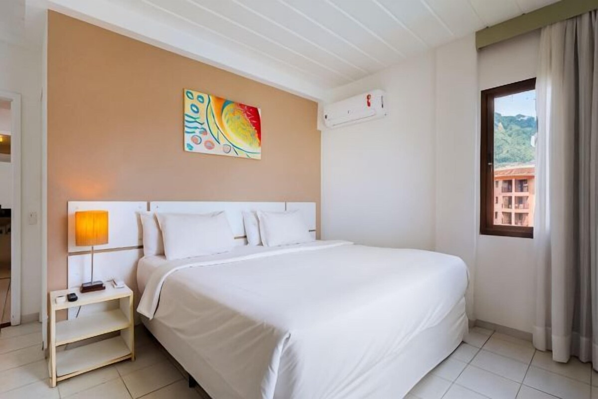 A hotel room with a bed, bedside table, lamp, and a window with curtains.