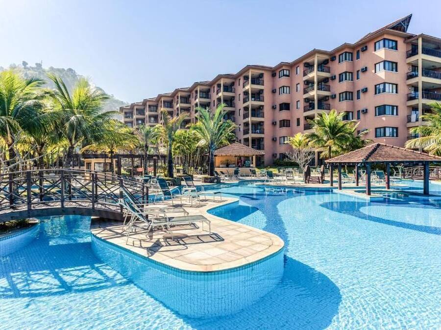 Un hotel con piscina, palmeras y montañas al fondo.