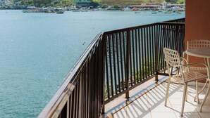 A balcony with a view of a lake and hills, featuring a table and chairs.