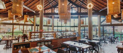 A spacious restaurant with high ceilings, large windows, and wicker hanging lights.