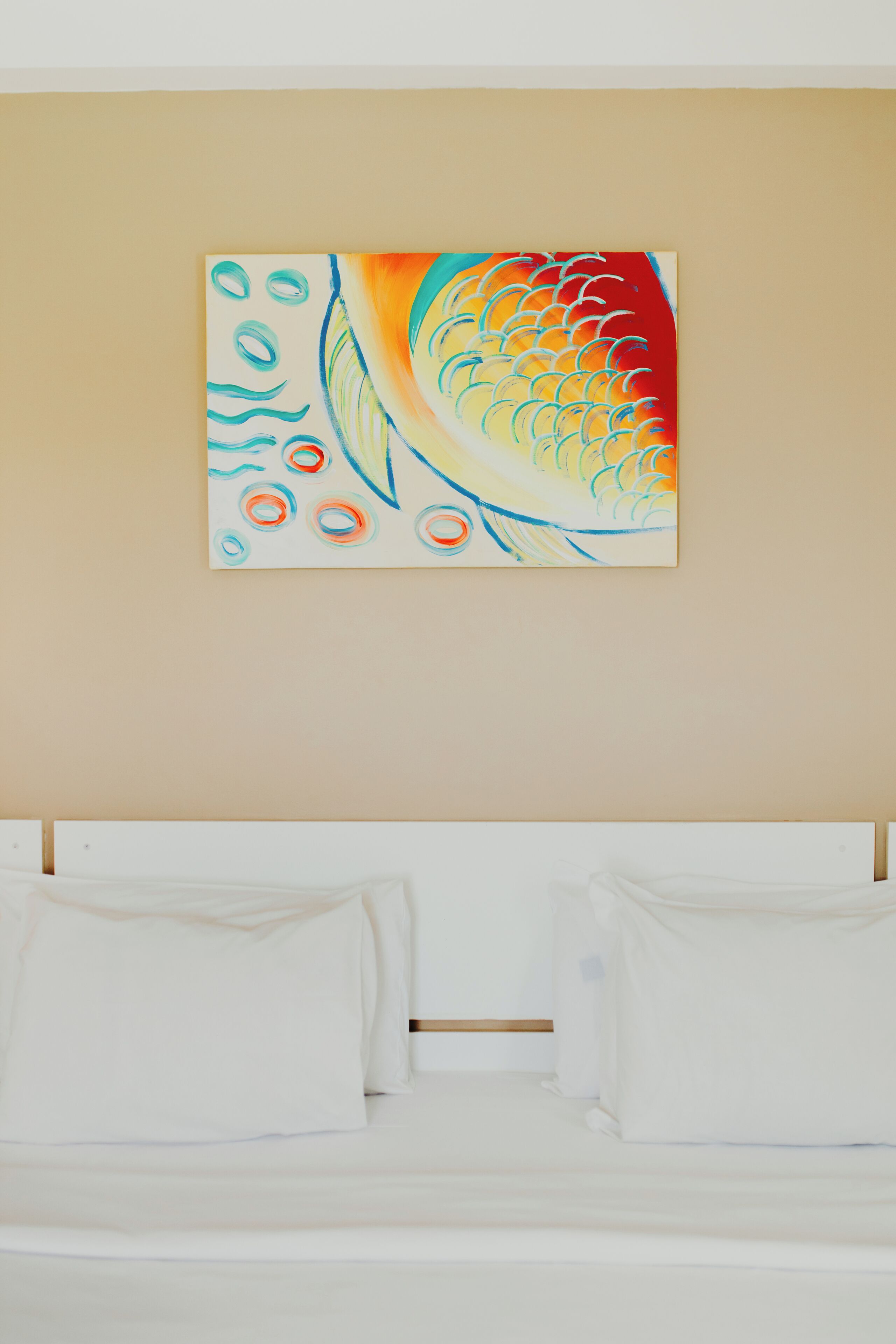 A room with a bed, white bedding, and a colorful abstract painting on the wall.