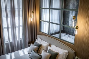 Camera d'albergo con un letto grande, vista su un bagno tramite una finestra e un lampadario fissato alla parete.