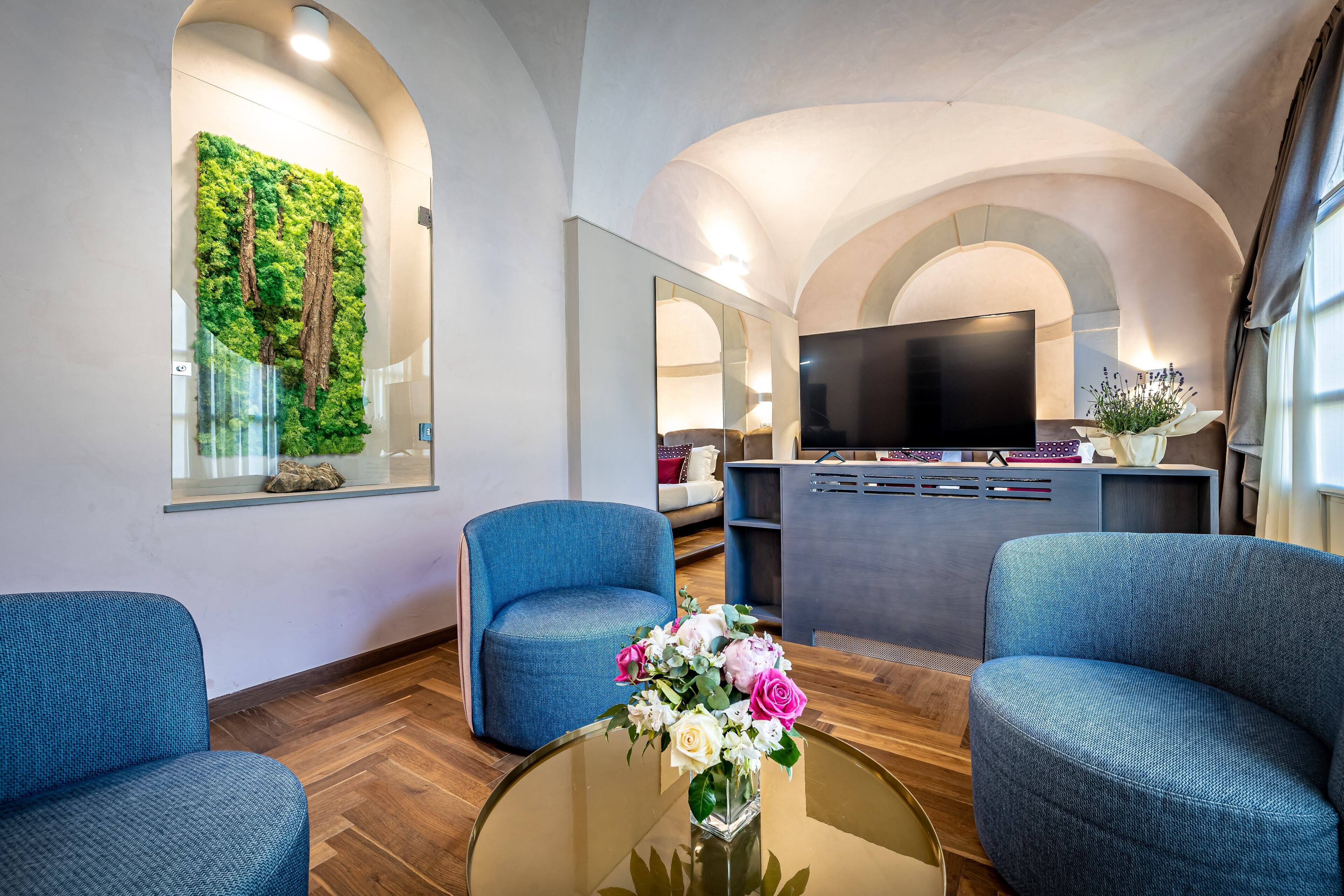 A modern living room with blue sofas, a glass coffee table, a flat-screen TV, and a green wall with vertical plants.