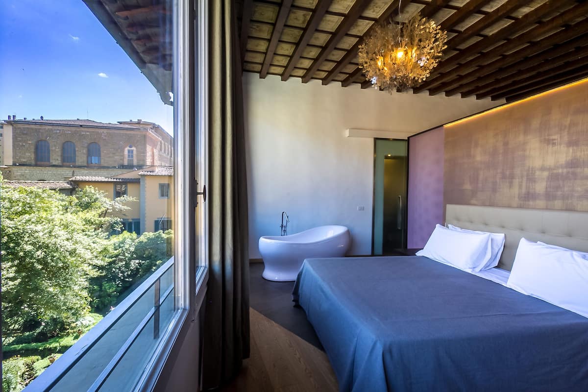 A modern bedroom with a large bed, a white bathtub, and a view of a cityscape.
