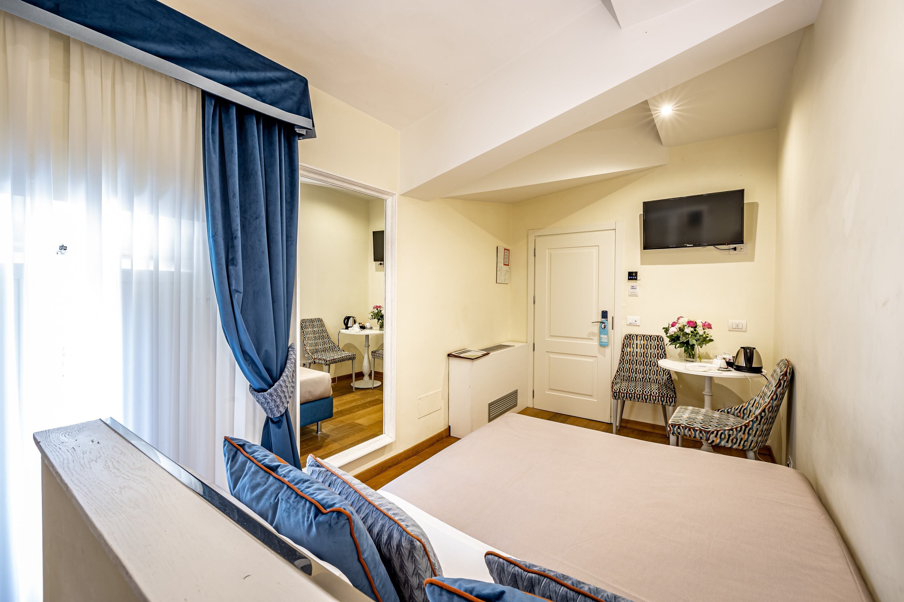 Een hotelkamer met een groot bed, een bureau met stoel, een televisie en een raam met gordijnen.