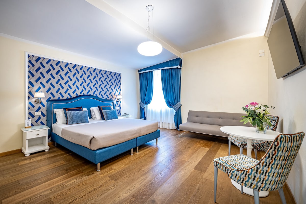 A bedroom with a bed, a nightstand, a sofa, a dining table, and chairs.