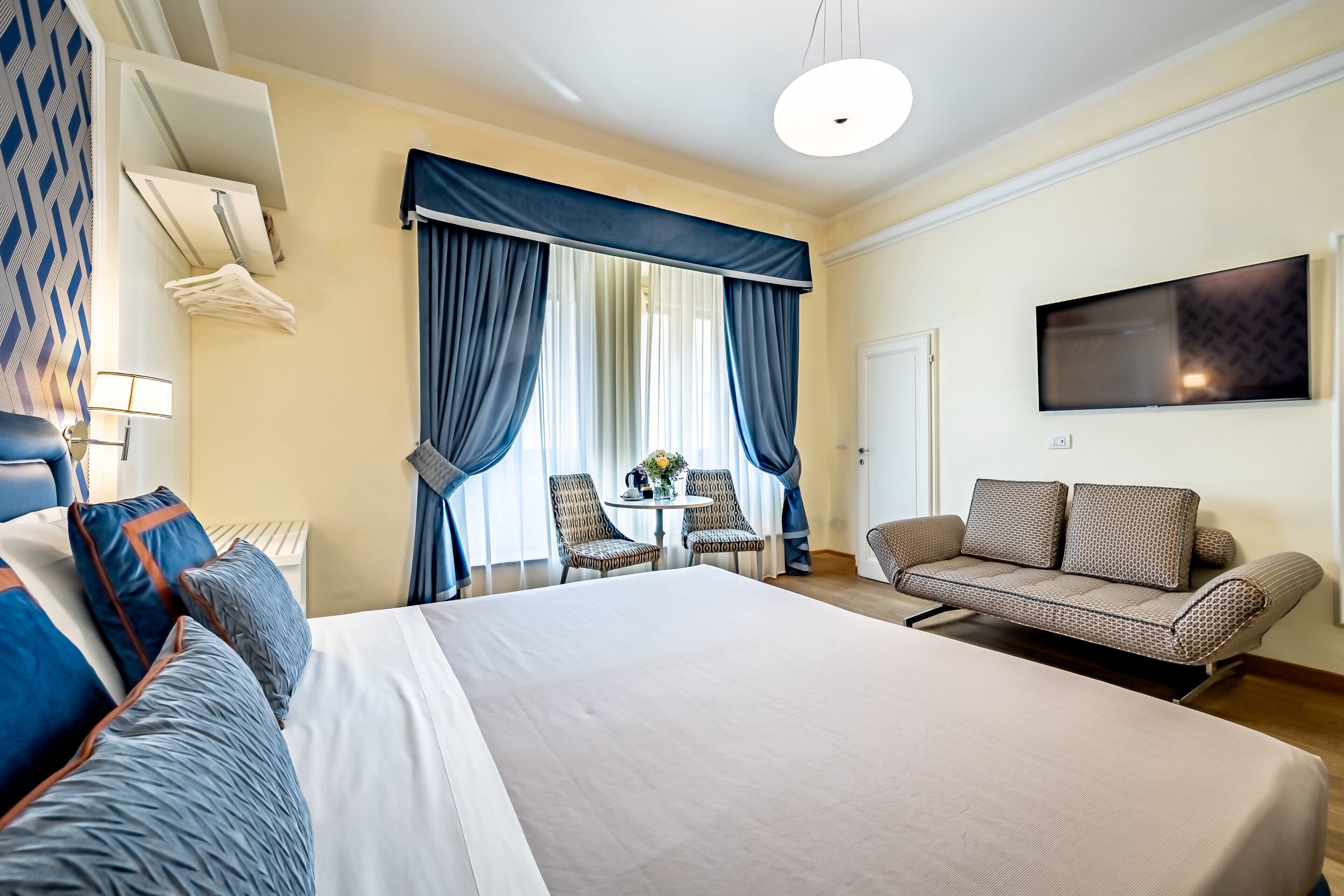 Ein Hotelzimmer mit einem großen Bett, einer Sitzecke, einem Fernseher und einem Essbereich mit Stühlen und einem Tisch.