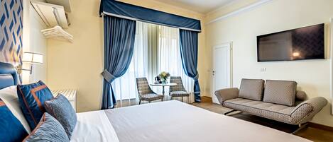 A hotel room with a large bed, a sofa, a TV, and a dining area with chairs and a table.