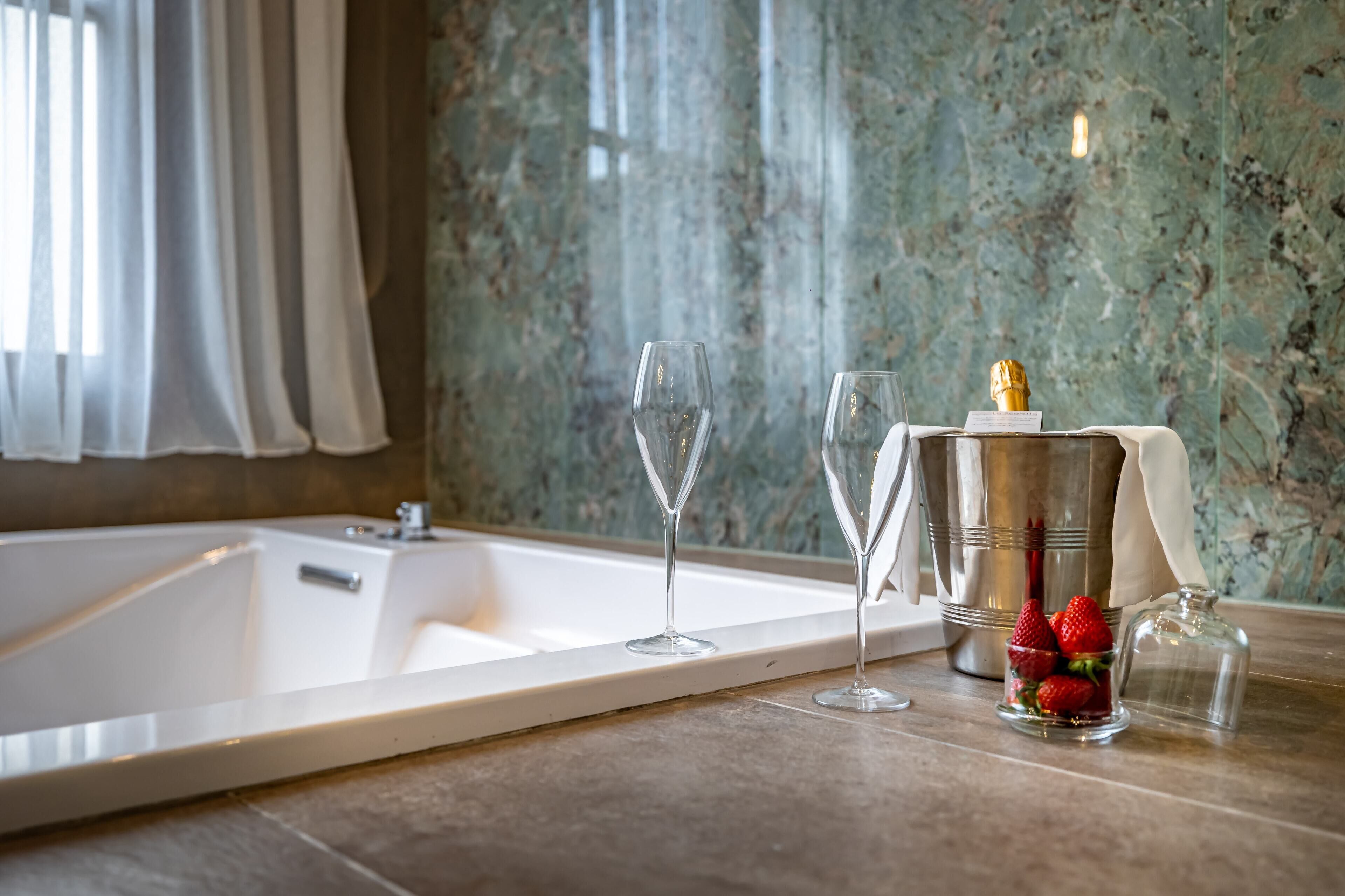 Une salle de bain avec une baignoire, deux verres à vin, une bouteille de champagne et un bocal en verre rempli de fraises.