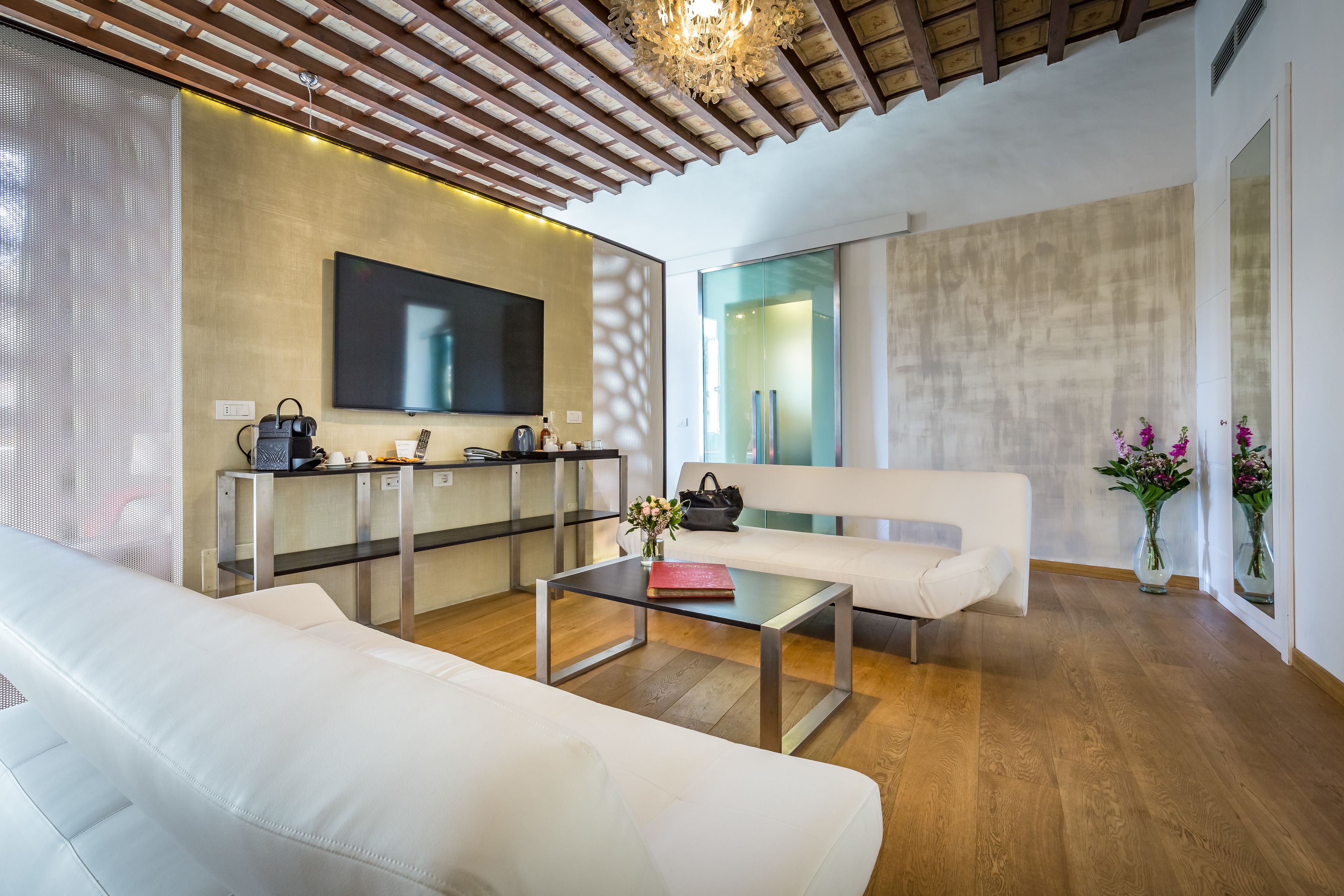 Una sala de estar moderna con un sofá blanco, una mesa de centro de vidrio y un televisor instalado en la pared.