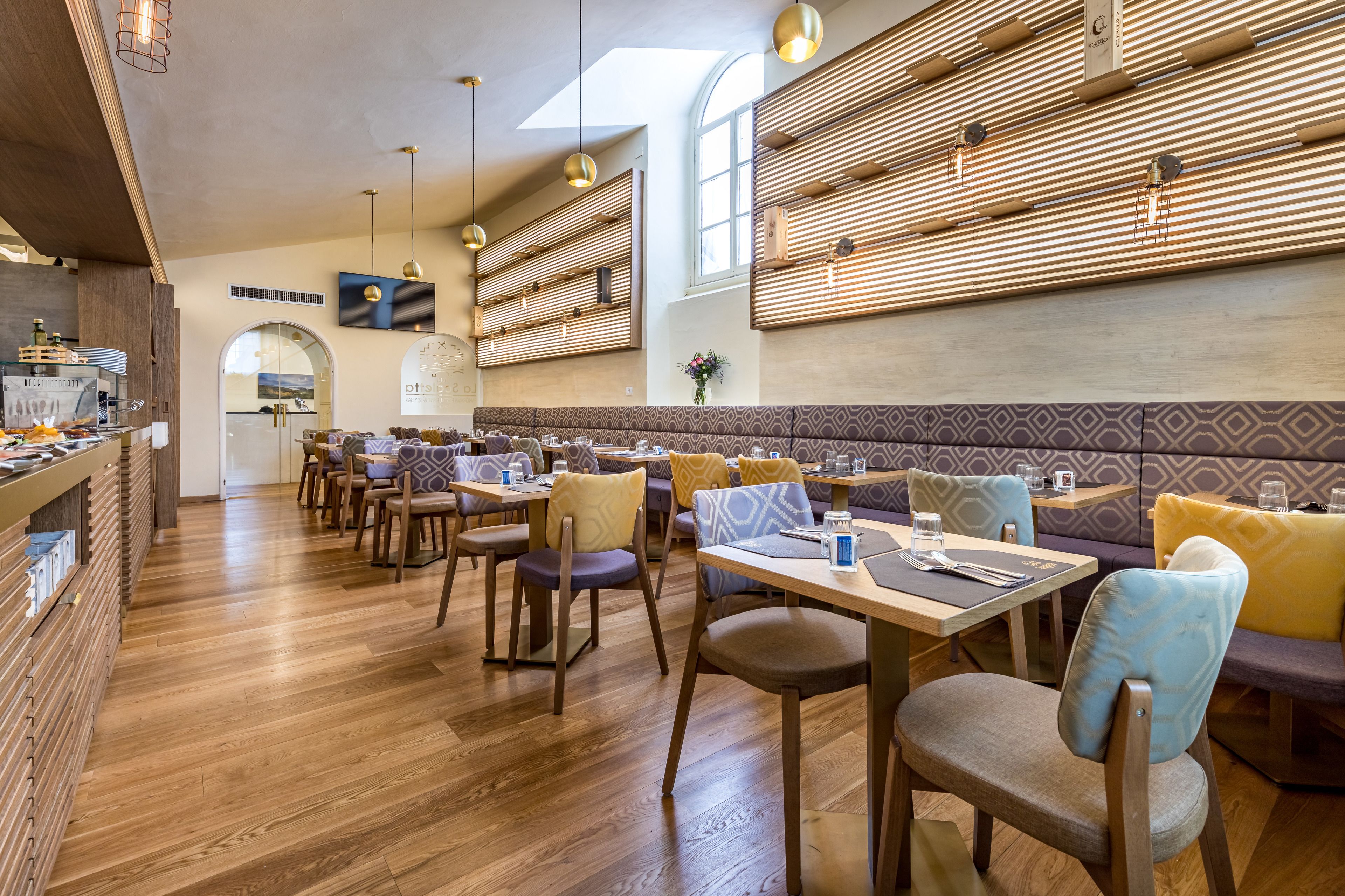 Un restaurant doté d’un plancher en bois, de plusieurs espaces de restauration, notamment des banquettes et des tables, et d’un aménagement intérieur moderne agrémenté de luminaires suspendus.