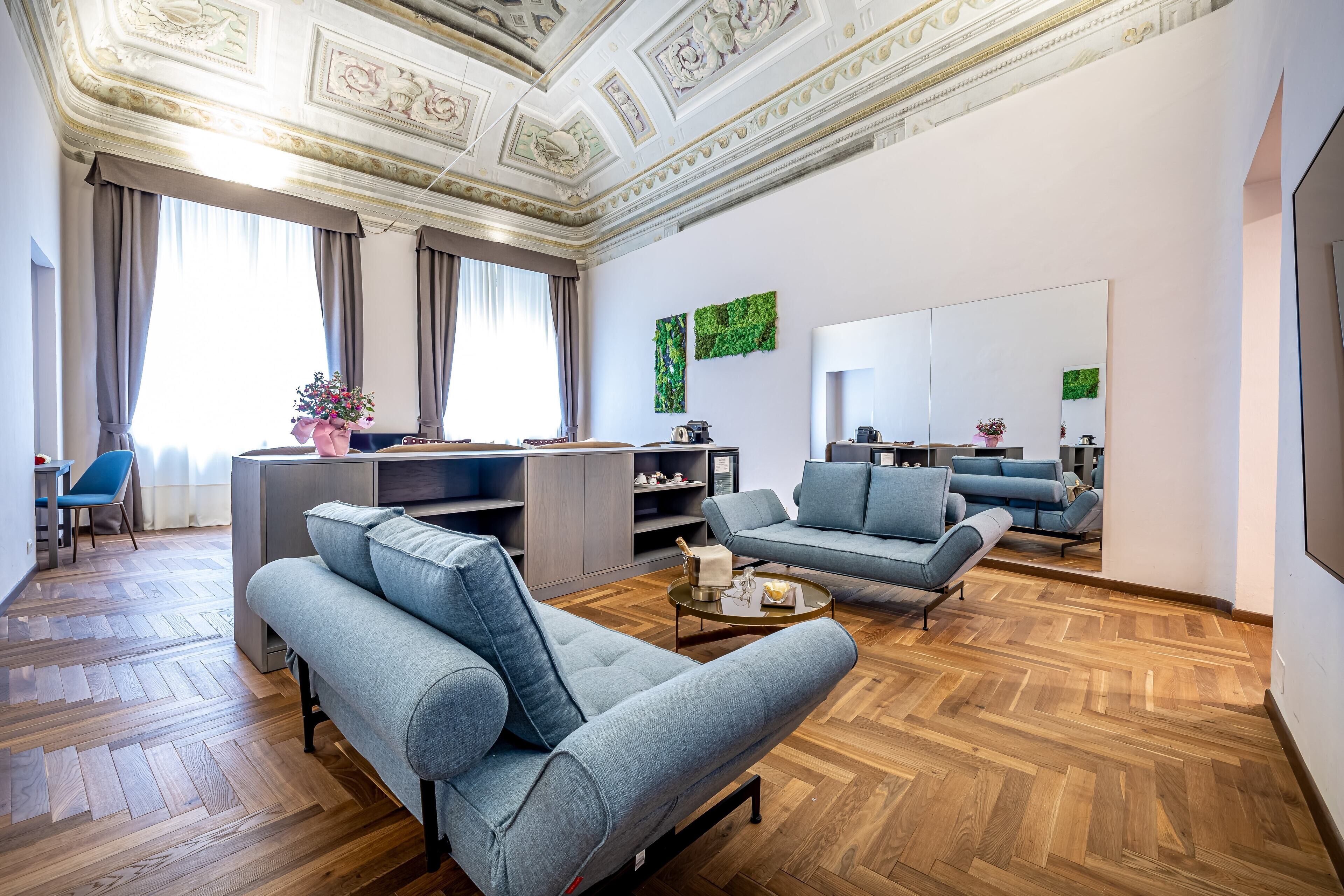 Una sala moderna con un sofá, sillones y una mesa de centro. Hay un escritorio con una computadora y una silla. El piso es de madera y el techo es decorativo.