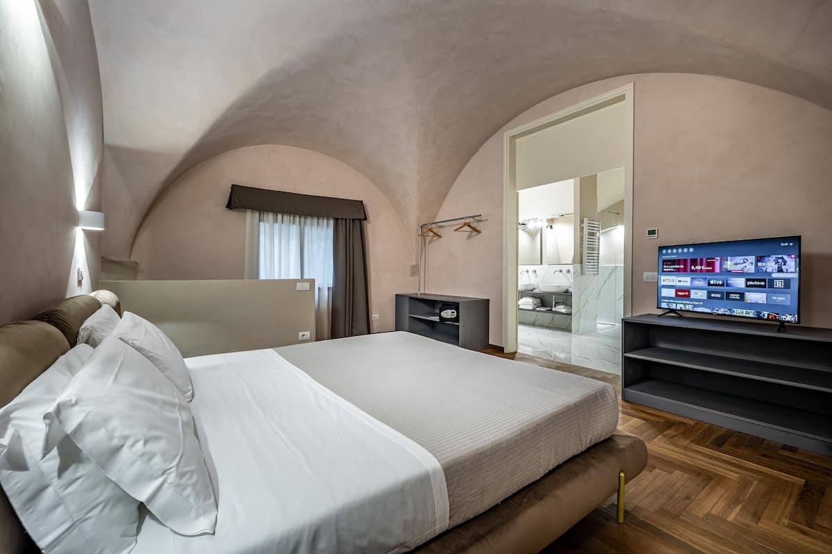 A bedroom with a large bed, a TV mounted on the wall, and a wooden floor.