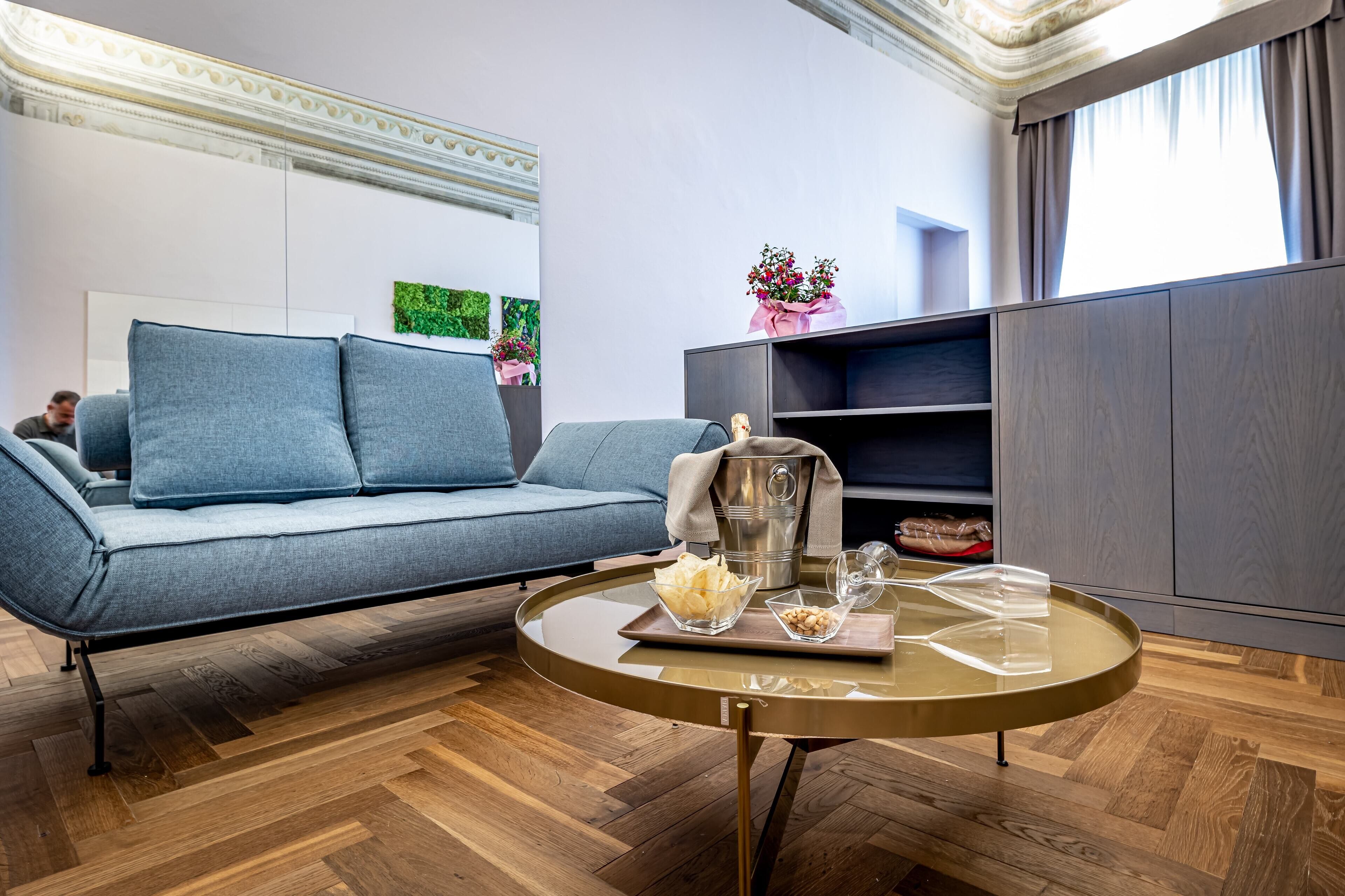 Ein modernes Wohnzimmer mit einem grauen Sofa, einem runden Couchtisch mit Tablett und einem Schrank mit einer Blumenvase.