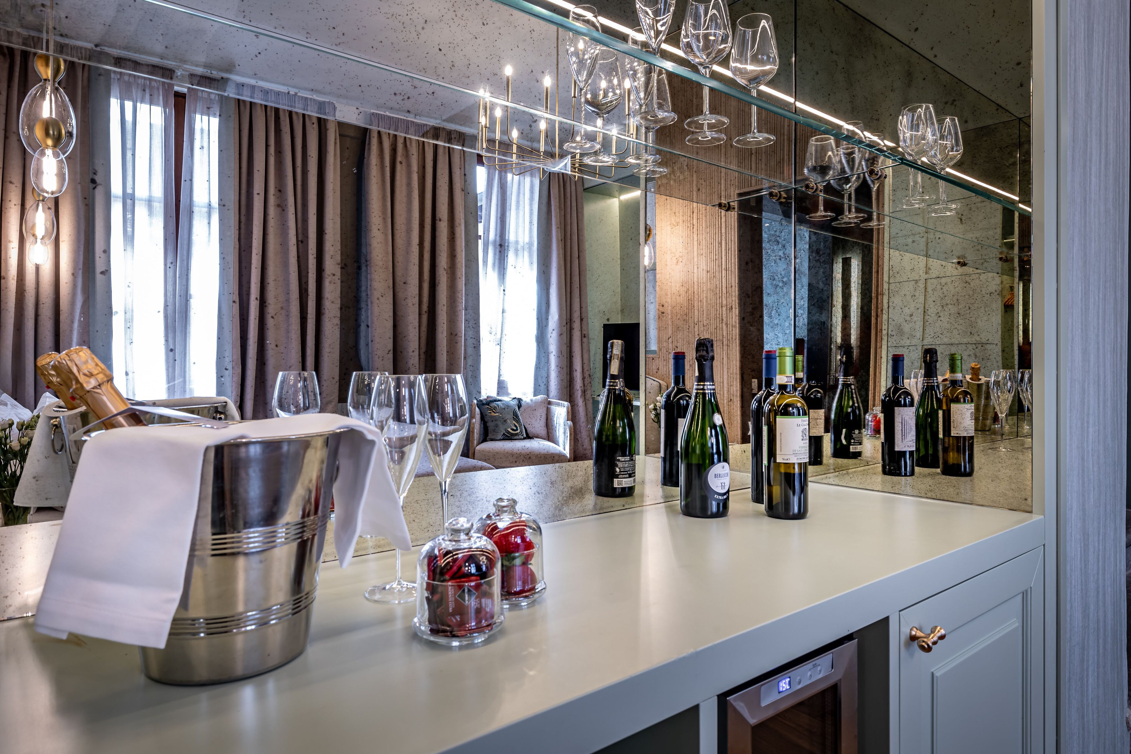 Un espace bar avec un présentoir à bouteilles de vin, un grand miroir et un coin salon comprenant un canapé et des rideaux.