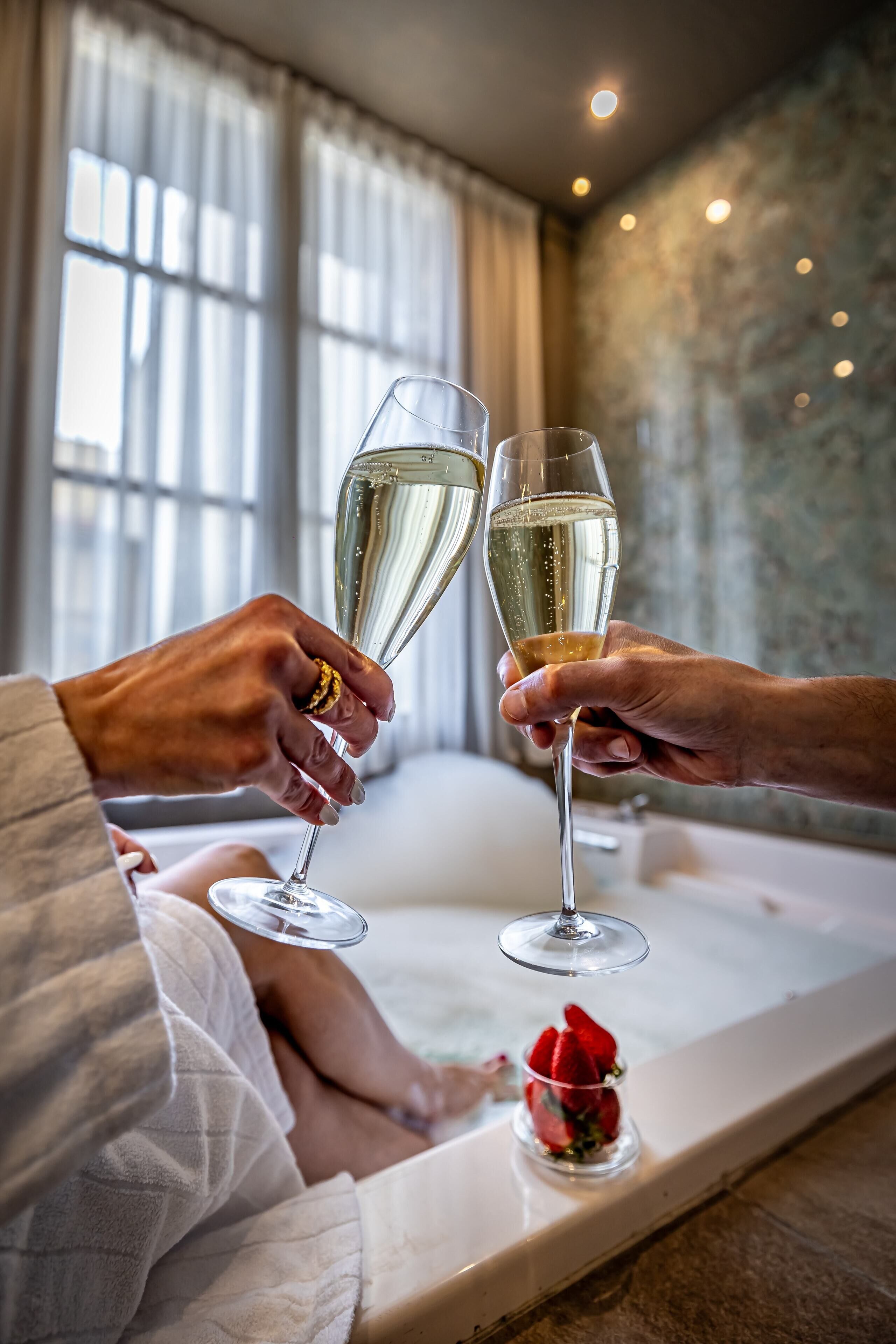 A person holding a champagne glass, another person holding a similar glass, and a small glass with a rose on a tray.