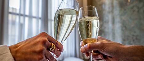 A person holding a champagne glass, another person holding a similar glass, and a small glass with a rose on a tray.