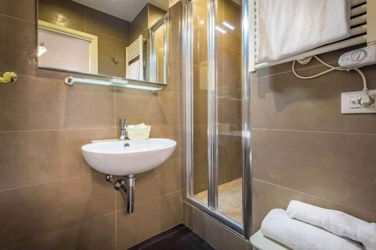 A bathroom with a sink, mirror, shower, and towel rack.