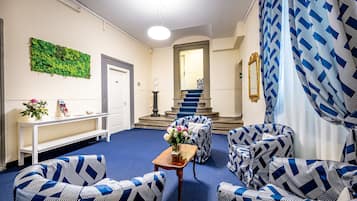 A lobby with patterned blue and white furniture, a green wall decoration, a staircase, and a reception desk.