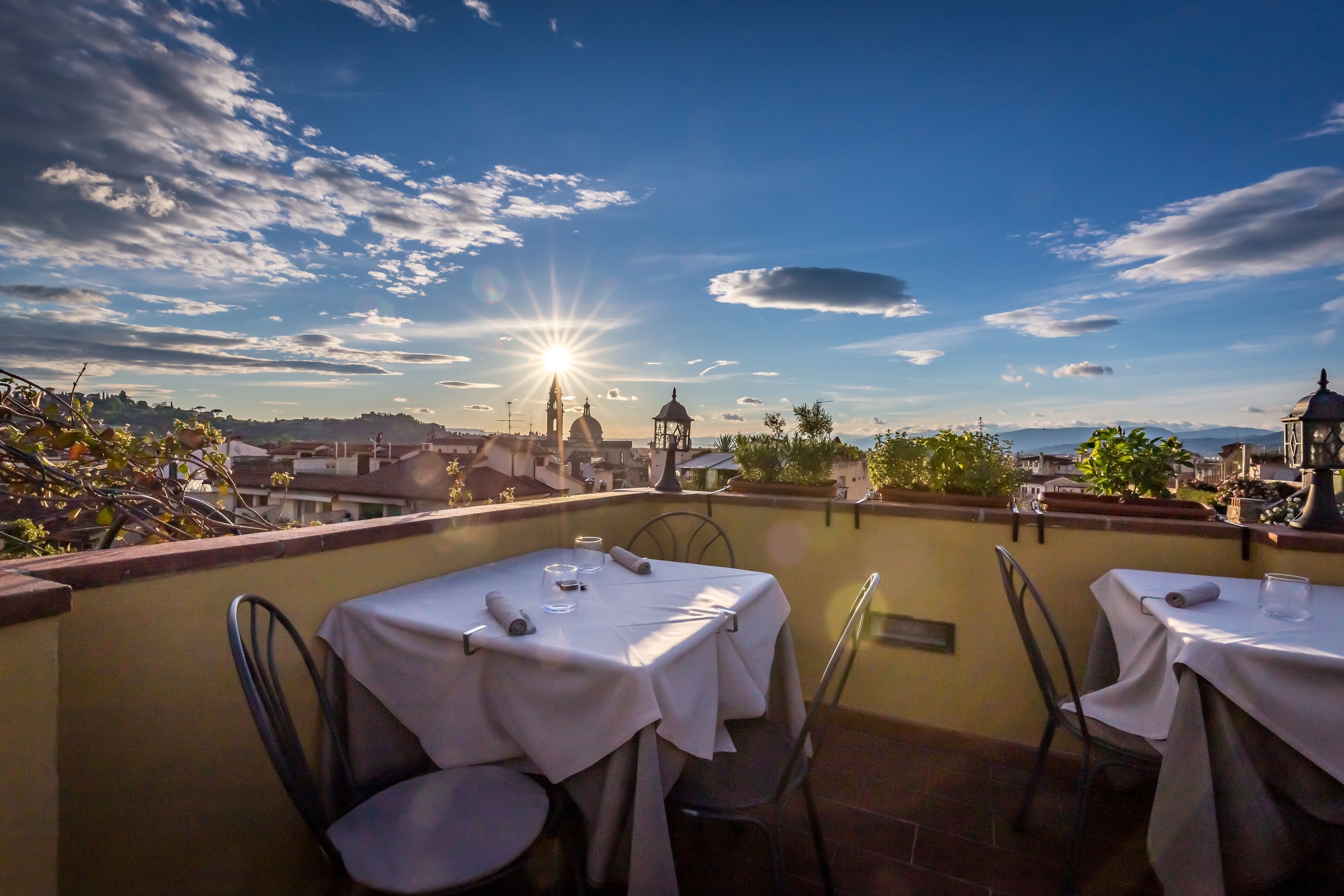 Eine Terrasse mit gedeckten Tischen, mit Blick auf eine Stadtlandschaft unter blauem Himmel und Sonnenschein.