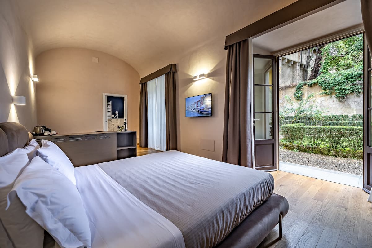 A bedroom with a large bed, a desk, and a view of a garden through an open door.