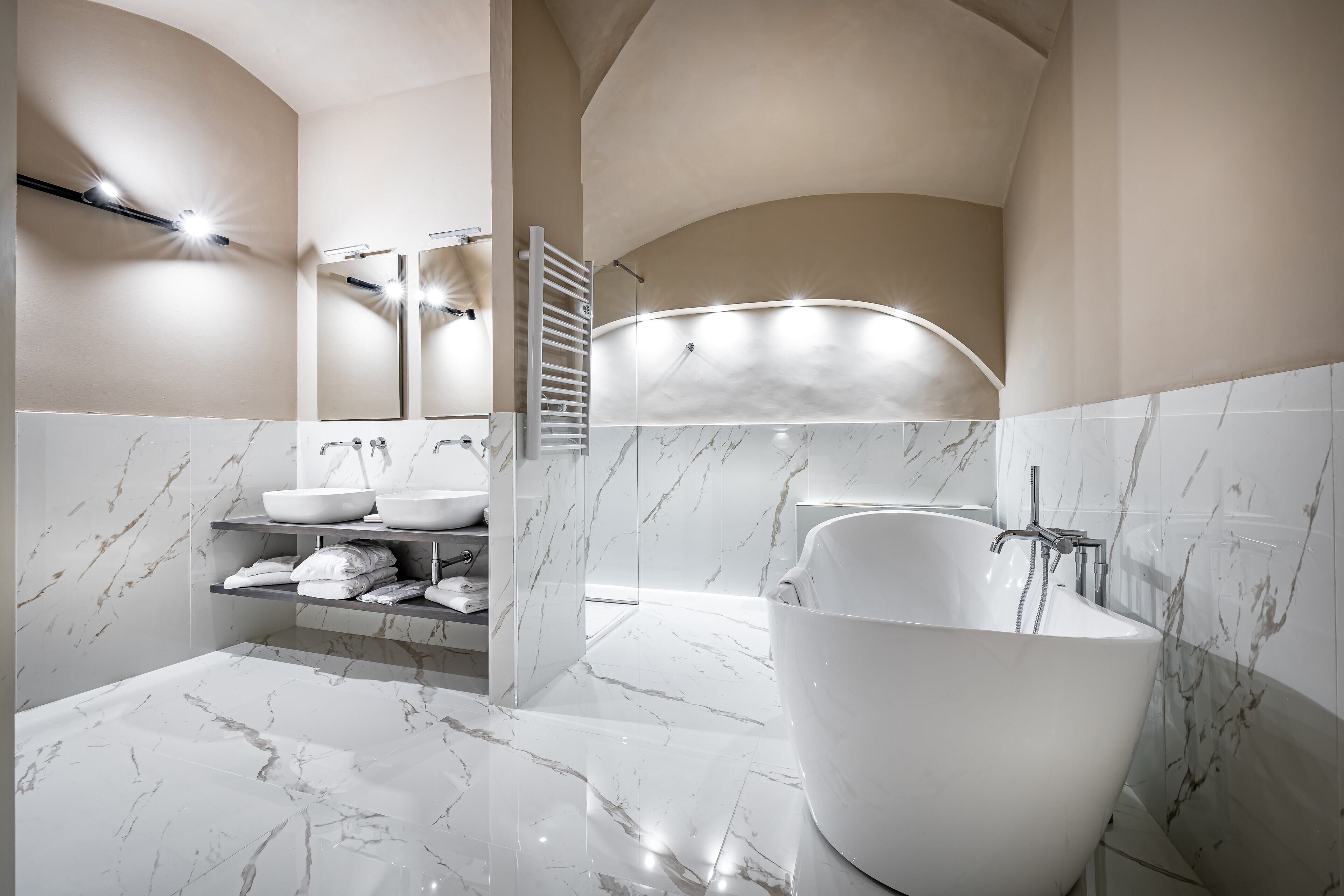 A modern bathroom with a freestanding bathtub, marble walls, and built-in shelves with towels.