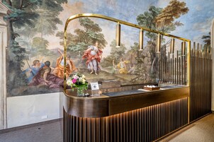 Una reception con un murale classico, una zona accoglienza moderna e un motivo decorativo in legno.