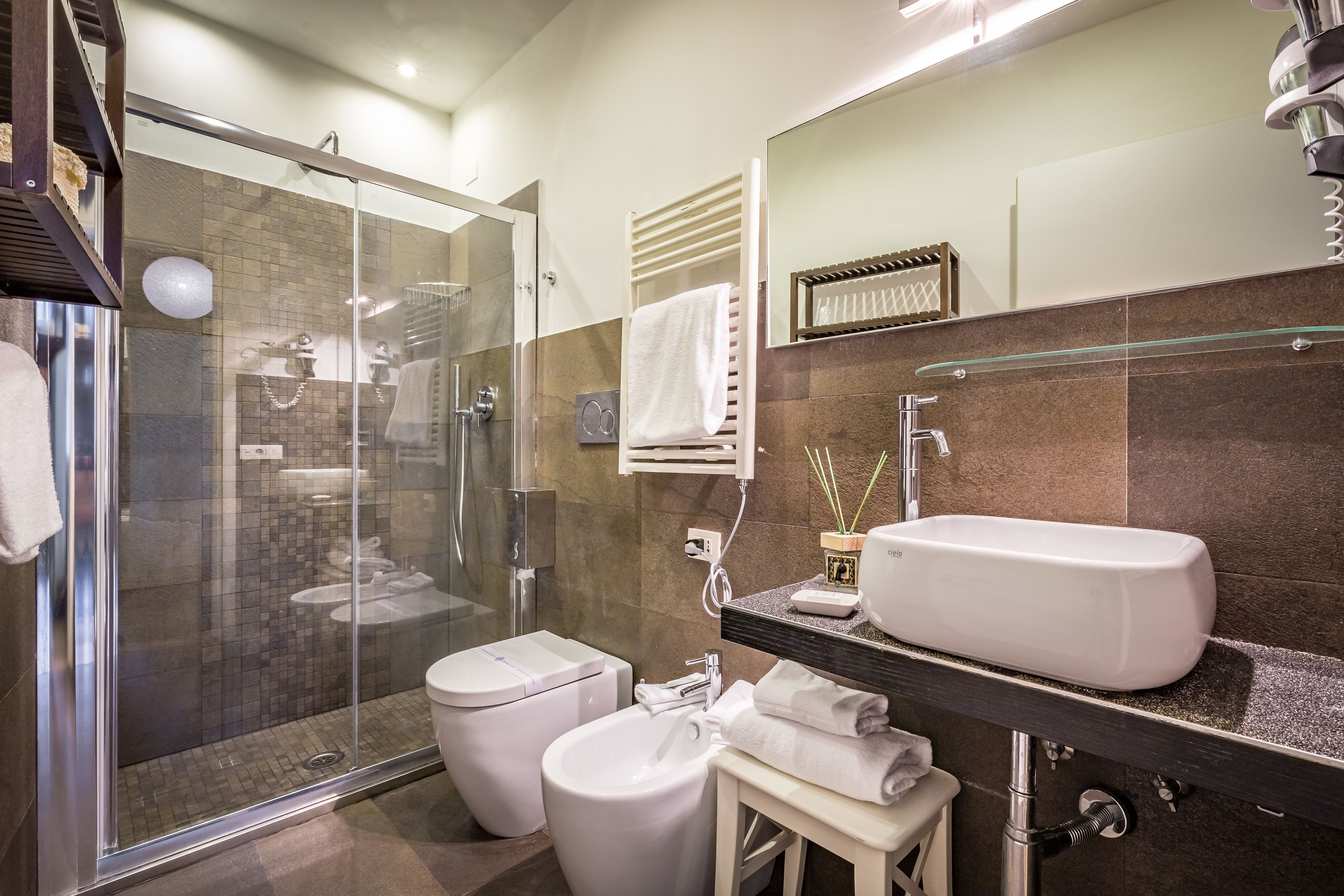 A modern bathroom with a glass shower enclosure, a toilet, a bidet, a sink, and a large mirror.
