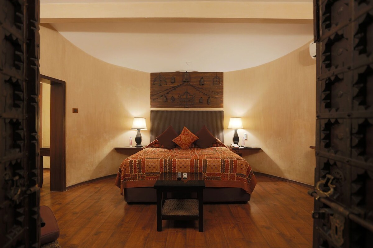 A bedroom with a bed, two bedside tables with lamps, a chair, and a wall-mounted artwork.