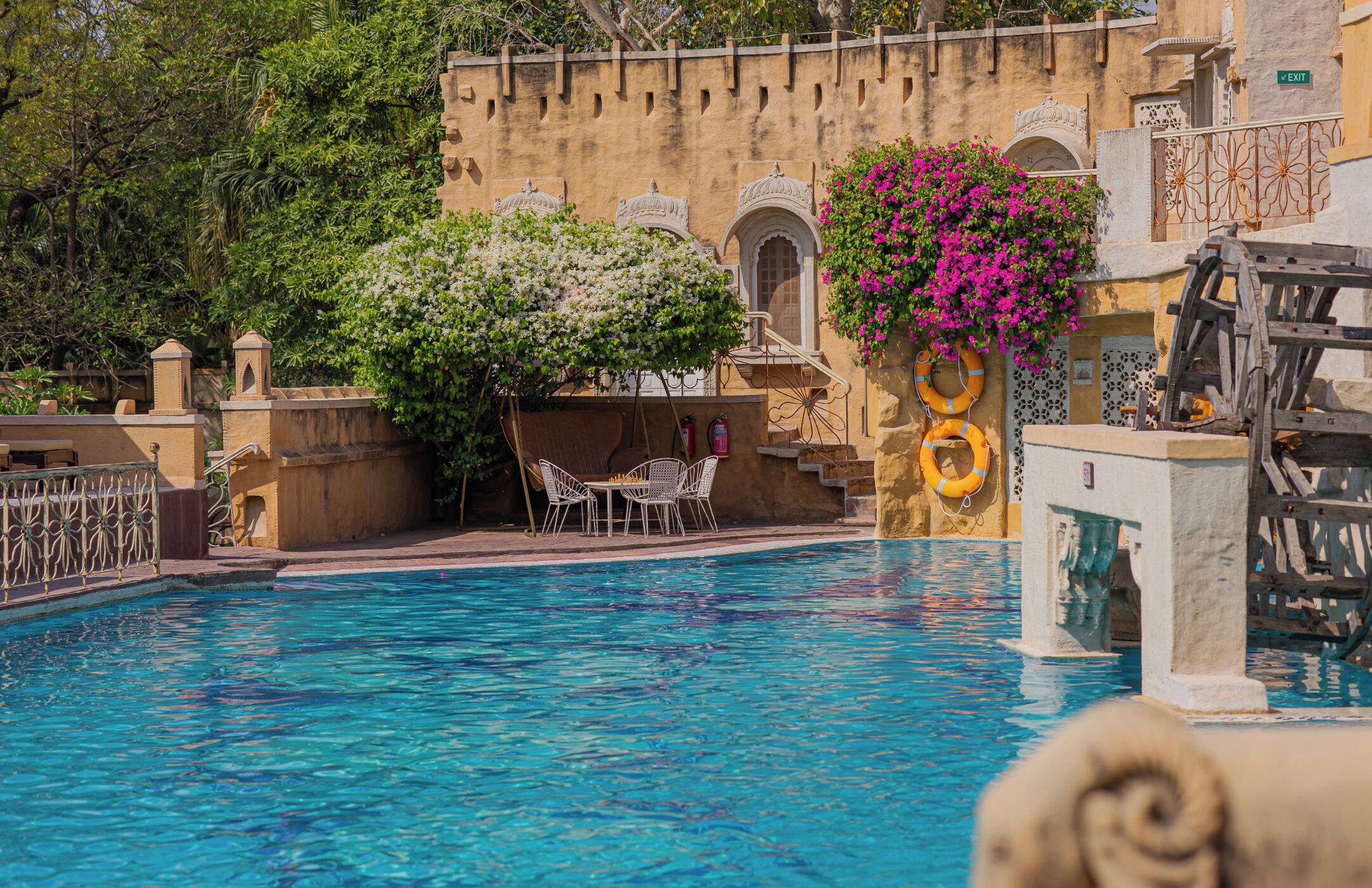 Piscina com um edifício tradicional ao fundo, um flutuador e uma roda d'água.