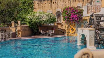 Piscina com um edifício tradicional ao fundo, um flutuador e uma roda d'água.