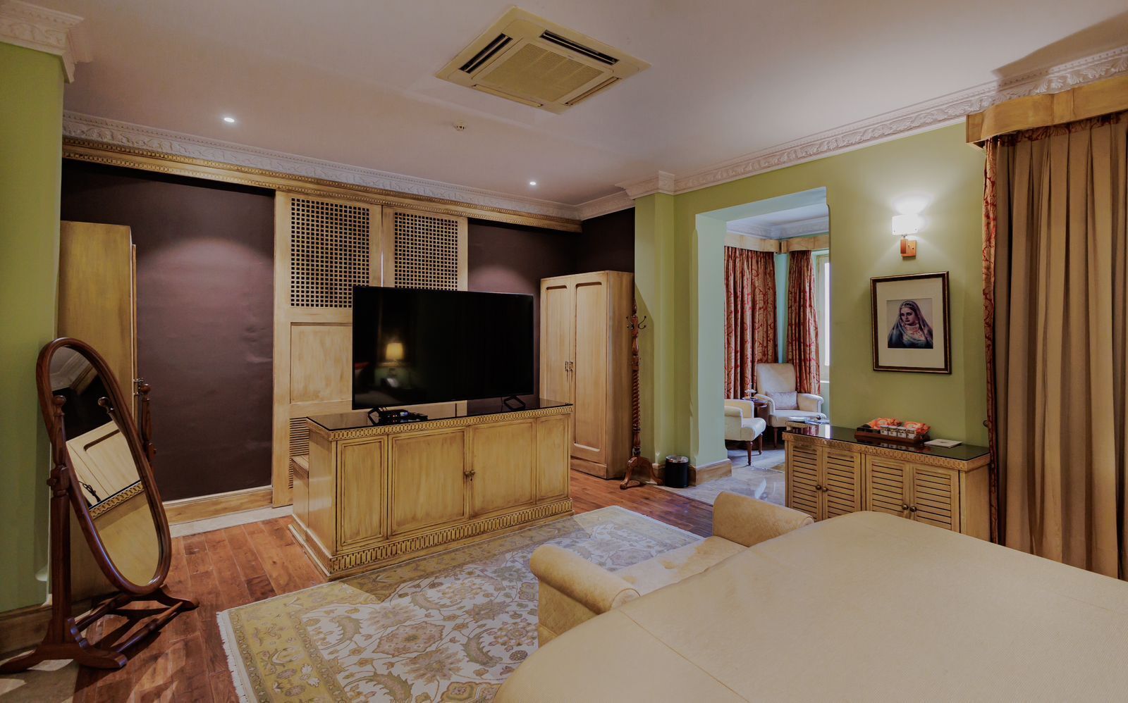 A hotel room with a large flat-screen TV, wooden cabinets, a dining table, and a patterned rug.