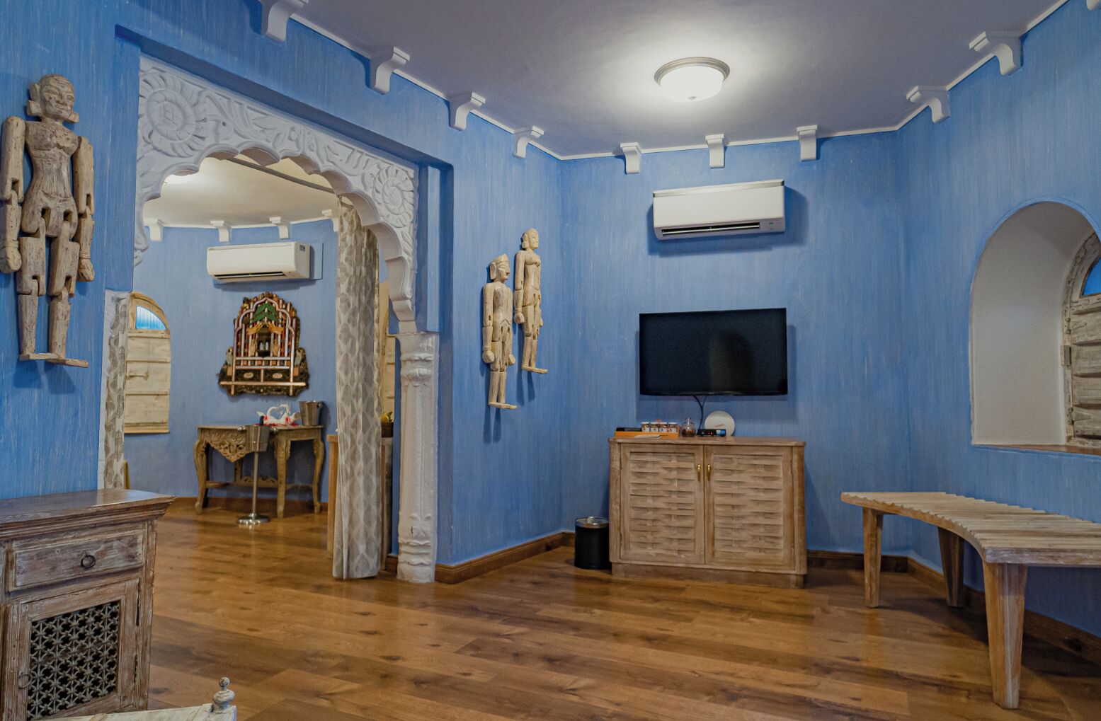 Una habitación con paredes azules, muebles de madera, un televisor y esculturas decorativas.
